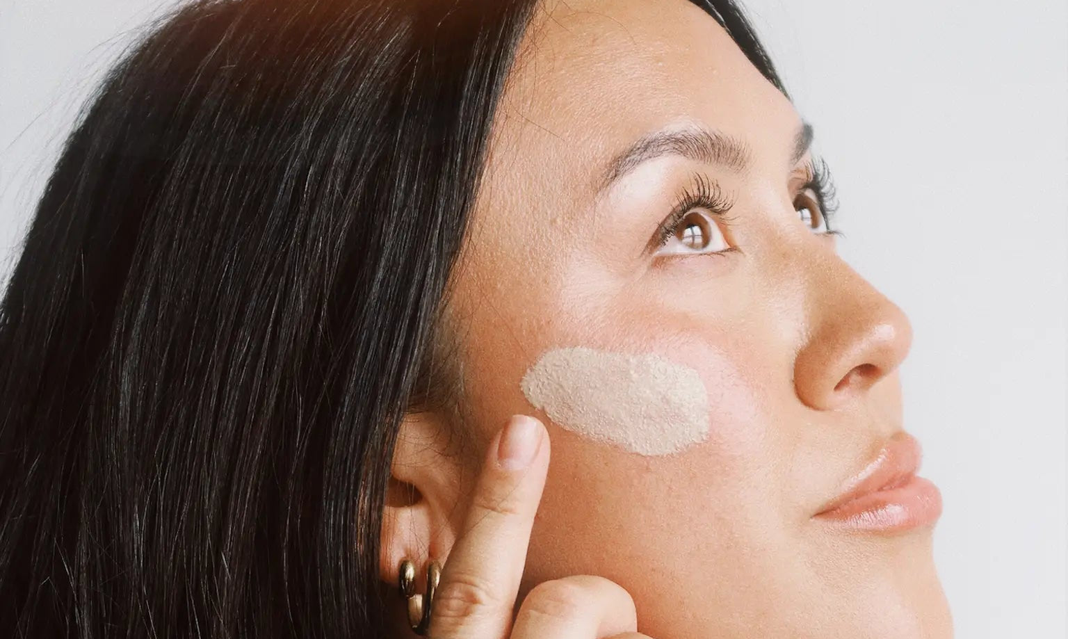 Woman applying cream to her face with a neutral background